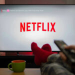Layoffs Hit Netflix Person watching Netflix with remote and drink.