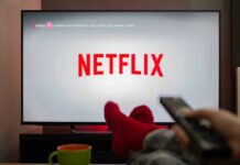Person watching Netflix with remote and drink.