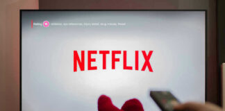 Person watching Netflix with remote and drink.