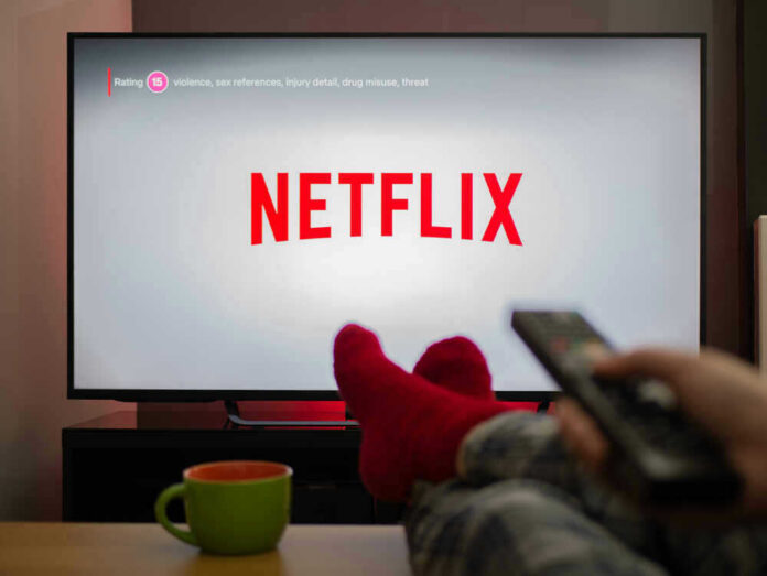 shutterstock_1683498799 Person watching Netflix with remote and drink.