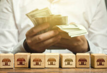 Person counting cash with wooden blocks depicting store icons