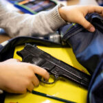 Kid placing handgun inside a backpack on desk