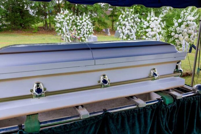 A,Funeral,Service,Is,Held,In,A,Cemetery,Followed,By A casket at a graveside surrounded by floral arrangements