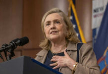 Hillary’s First Midterm Shot Lands Hillary Clinton speaking at a podium with a microphone
