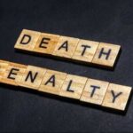 Firing Squad Twist – Date Set Wooden letter tiles spelling DEATH PENALTY on a dark background