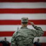 A military personnel saluting in front of a large American flag