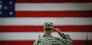 A military personnel saluting in front of a large American flag