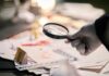 Gloved hand holding a magnifying glass over scattered forensic documents