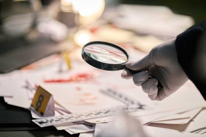 Gloved hand holding a magnifying glass over scattered forensic documents