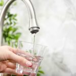 Longevity Drinks Exposed: Just Three Hand holding a glass under a kitchen faucet as water pours in