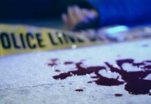 Blood on pavement with police tape and a hand in the background