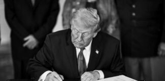 man in suit signs a document at a desk