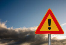 WATCH: Dozens Dead in High-Speed Horror A triangular warning sign with an exclamation mark against a cloudy sky