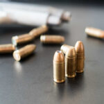 Superstar’s Home Riddled By Bullets – Nursery Hit Close-up of bullets on a dark surface with a handgun in the background
