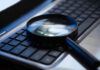 Terrifying Clue Hiding In Your Voice Magnifying glass on a laptop keyboard.