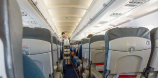 Airplane cabin aisle with rows of seats and a flight attendant pushing a service cart